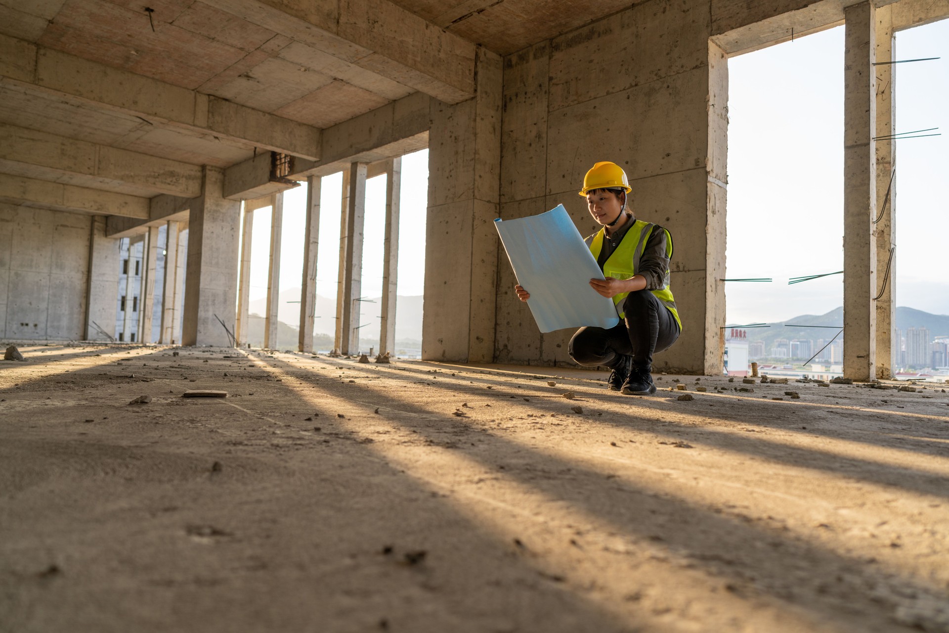 The sun shines through the real estate space, and a female engineer is checking the construction site with drawings